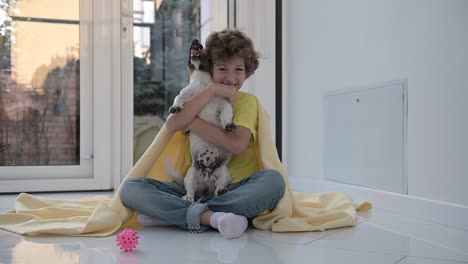 blond boy with curly hair sitting on the floor hugging his dog