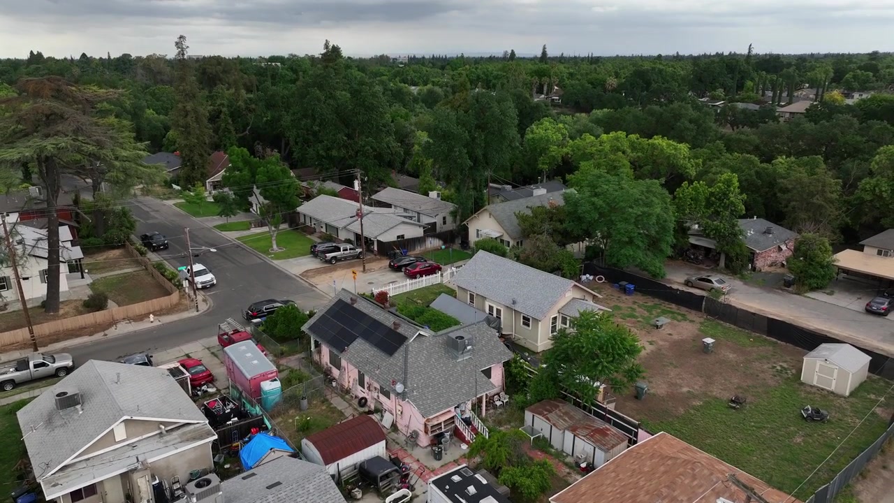 Quartiere residenziale a Modesto, California, con case suburbane dotate di pannelli solari e alberi verdi e rigogliosi lungo una strada tranquilla durante una giornata nuvolosa nella Central Valley, USA. Ripresa aerea in ascesa