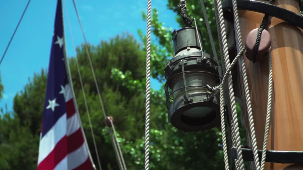 Tight shot of lantern and mast with 13 star American flag out of focus on old 17th century sailing ship