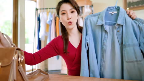 Portrait-confident-Asian-young-woman-is-online-small-business-owner-sitting-on-couch-and-live-streaming-to-online-for-selling-clothes-by-smartphone-at-home-office