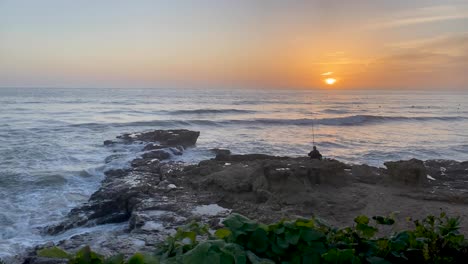 An-experienced-fisherman-trying-to-fish-with-a-professional-spinning-rod-on-the-rocks-with-the-lapping-sea