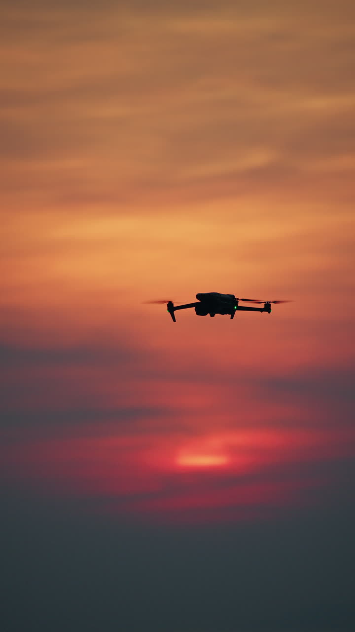 Dronesilhuet flyver mod en farverig solnedgangshimmel over en rolig havhorisont.