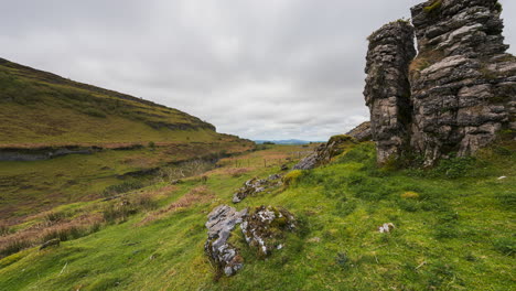 Panorama-Bewegungszeitraffer-Von-Ländlichem-Natur-Ackerland-Mit-Felsbrocken-Im-Vordergrund,-Grasfeld-Und-Hügeln-In-Einer-Talentfernung-Während-Eines-Bewölkten-Tages,-Gesehen-Von-Carrowkeel-In-Der-Grafschaft-Sligo-In-Irland