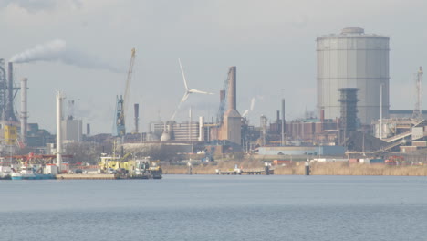 windmill standing on a polluting industrial terrain located near river