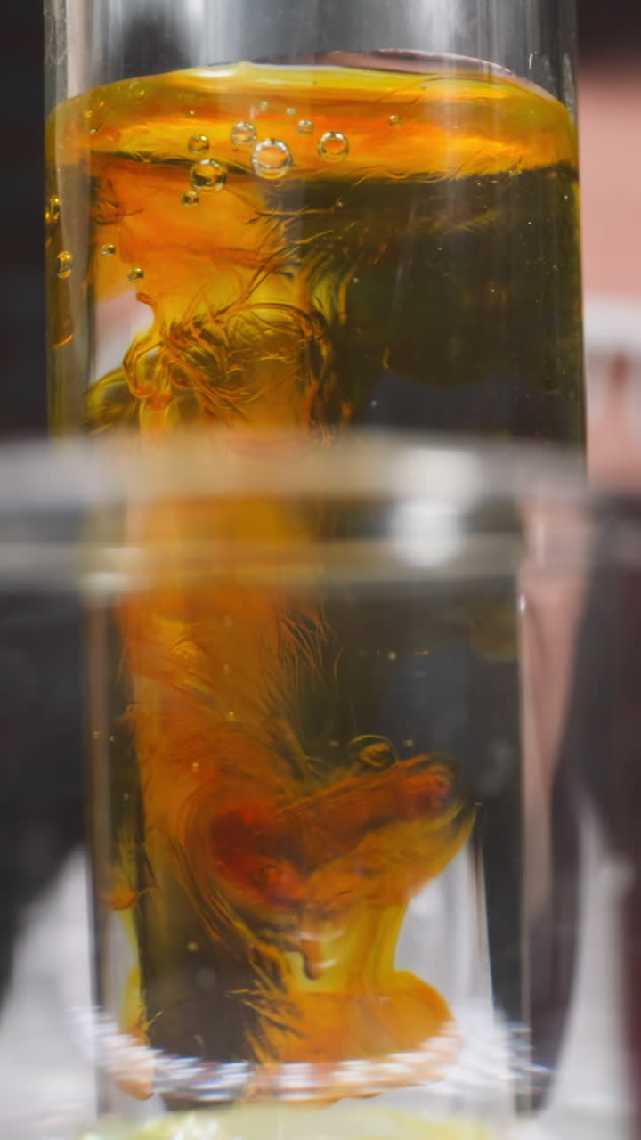 Drops of orange chemical reagent fall down into test tube under woman control in lab slow motion. Probe lens shot of chemical solutions macro