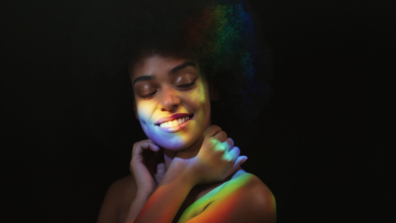 ritratto multicolore ravvicinato bella donna afroamericana con afro che gode di una pelle liscia e sana che sembra sicura bellezza naturale luce colorata su sfondo nero concetto di cura della pelle