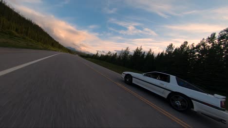 a white sports car driving down highway filmed with a drone. the opening shot starts with the drone flying through a road sign as the drone closes in on the car.