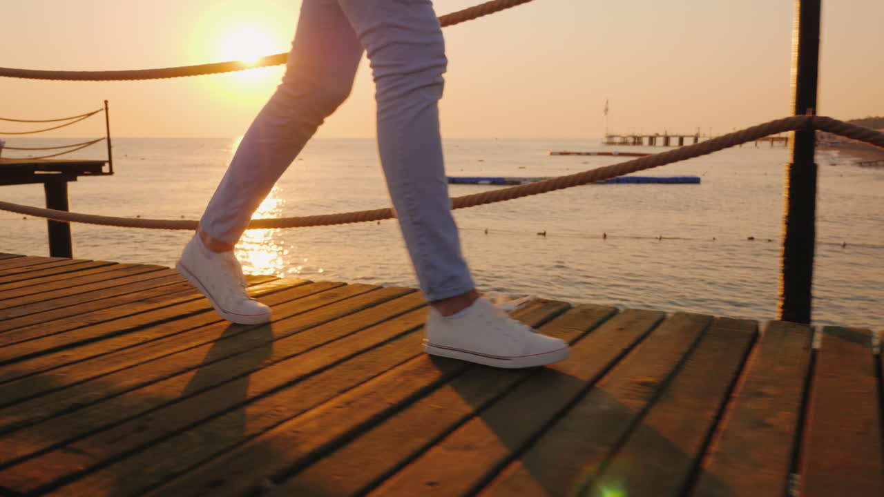 여자는 다리만 스테디캠으로 볼 수 있는 프레임에서 이른 아침에 부두를 따라 걷는다