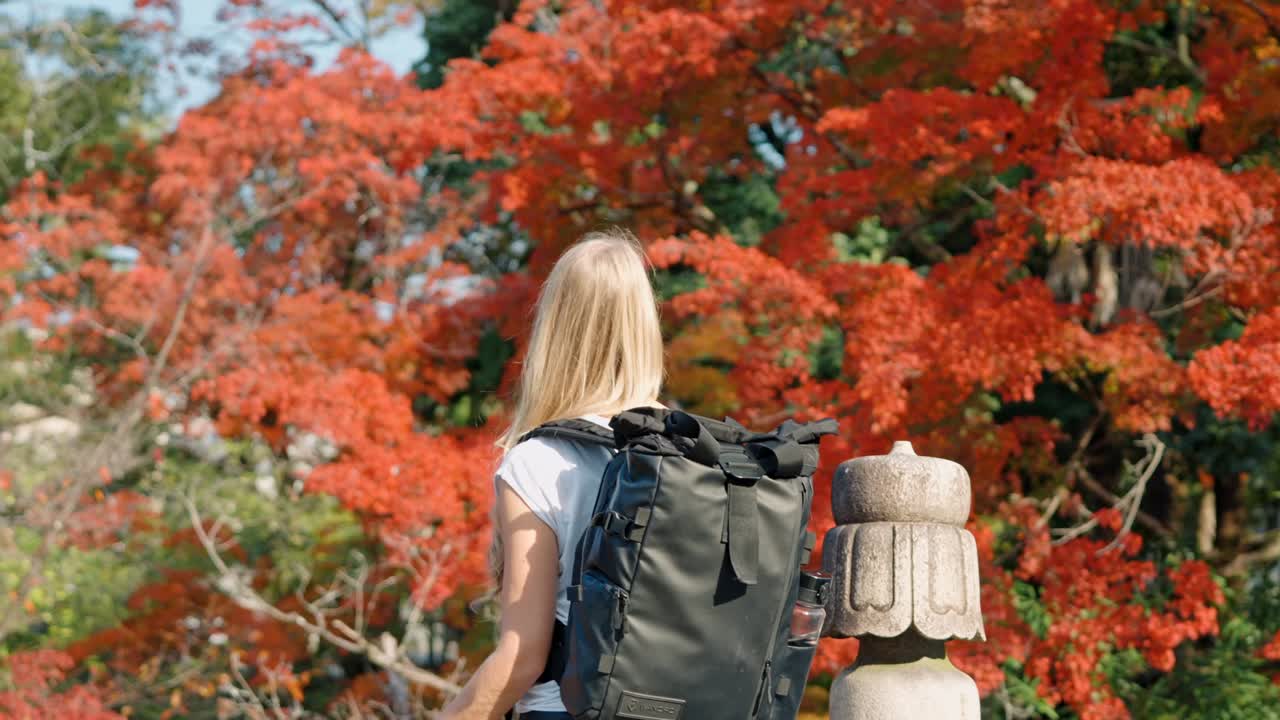 A young woman stands on a wooden bridge in Kyoto, Japan, gazing at the breathtaking red autumn foliage.