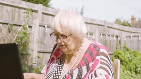 elderly woman typing on a black laptop outside in the garden day