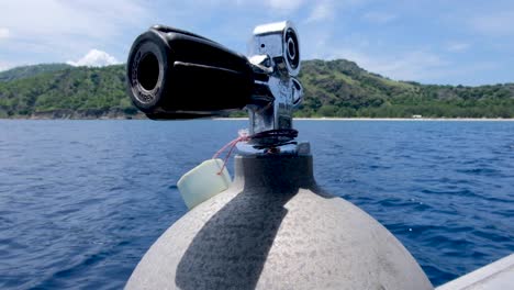 A-scuba-divers-oxygen-tank-primed-and-ready-for-action-on-a-rocking-dive-boat-on-blue-ocean-with-tropical-island-backdrop