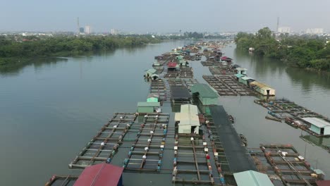 drone-shot-flying-over-floating-fish-farming-community-in-Bien-Hoa-on-the-Dong-Nai-river,-Vietnam-on-a-sunny-day