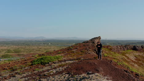 Aerial-view-of-man-explorer-backpacker-using-smartphone-standing-rock-formation-in-Iceland.-Drone-view-of-young-man-tourist-technology-addicted-ignoring-panorama-surfing-web