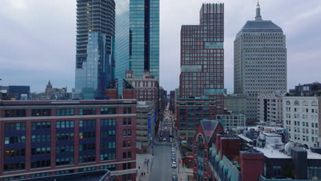 Volar-Por-Encima-De-La-Calle-En-La-Ciudad.-Hacia-Atrás-Revelan-Edificios-Altos-De-Oficinas-En-El-Centro-Y-Grúas-Torre-En-El-Sitio-De-Construcción.-Boston,-Estados-Unidos