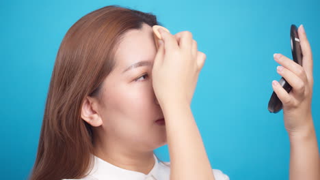 파란색 배경에 웰빙 피부 관리를 위해 파우더 얼굴을 적용하는 아시아 여성의 닫습니다