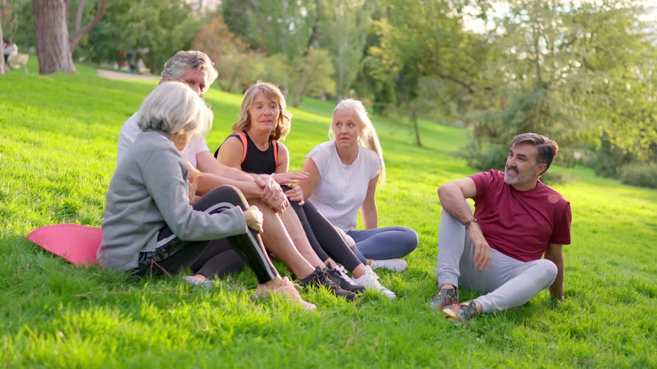 Gruppe af modne venner, der sidder og snakker på græs i parken