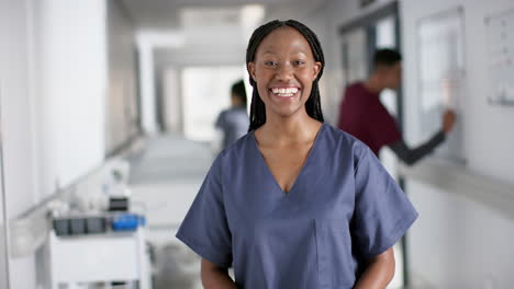 Portrait-of-happy-african-american-female-doctor-wearing-scrubs-in-hospital,-slow-motion