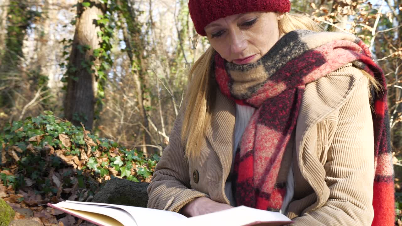 primer plano dando vueltas, mujer con ropa de invierno sentada leyendo un libro en el bosque