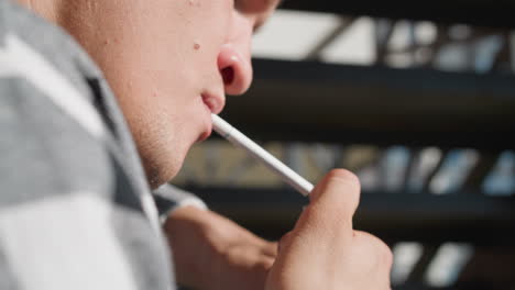 close up of man holding cigarette in mouth struggling to ignite lighter as frustration builds, lips pursed and jaw clenched, with blurred urban background