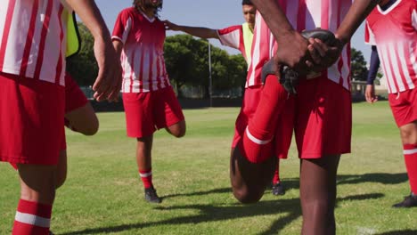 Video-of-diverse-group-of-male-football-players-warming-up-on-field,standing-and-stretching-legs