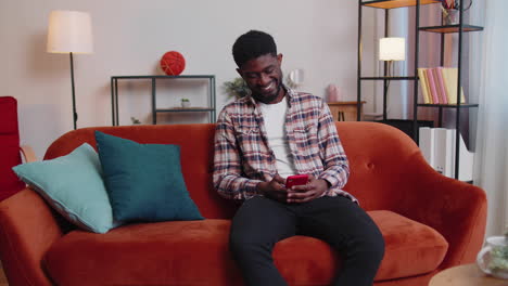 cheerful young man sitting on sofa, using mobile phone share messages on social media application