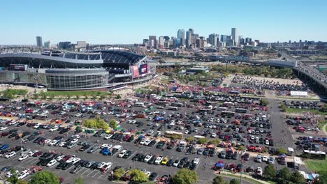 cinematic aerial shot of empower field at mile high stadium with lots of cars parked in parking spaces and main street highway and downtown denver city view backdrop, colorado