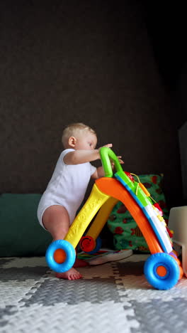 adorable plump baby wearing white body suit is at home. child stands holding by the walker and suddenly drops on the floor. vertical video.