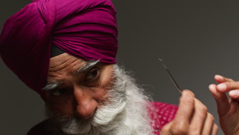 close up low key studio lighting shot of senior sikh man with beard using salai needle when putting on turban against dark background 3