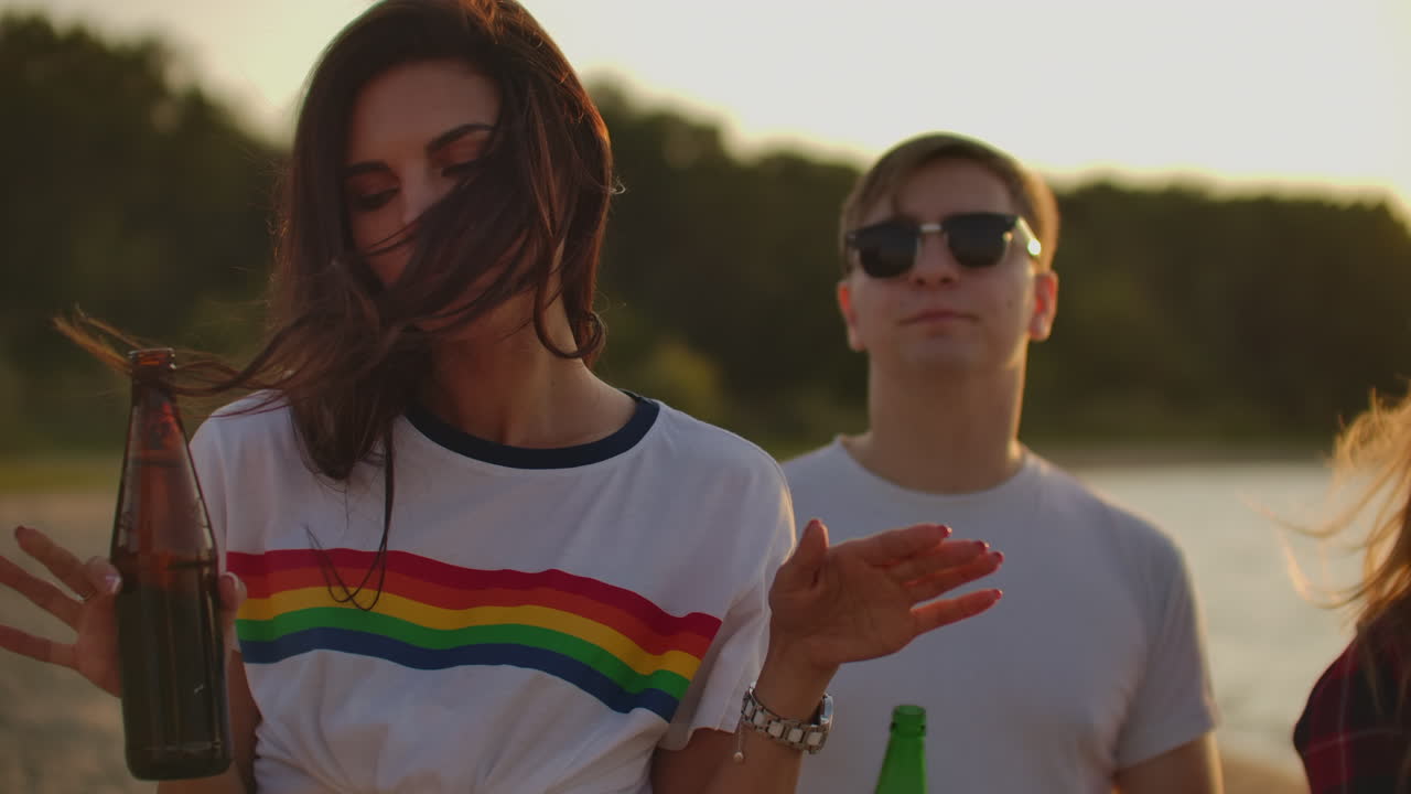 Female from company of young people celebrate the end of the semester with beer. This is carefree summertime. They dance and drink beer on the open air party.