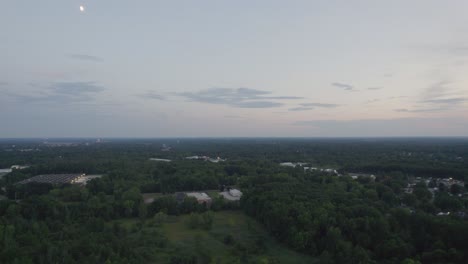 Luftdrohnenaufnahme,-Die-Während-Der-Abendzeit-Nach-Sonnenuntergang-über-Einer-Stadt-Schwebt,-Die-Von-üppiger-Grüner-Vegetation-Umgeben-Ist