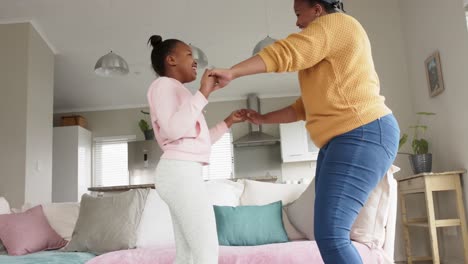 Happy-african-american-mother-and-daughter-having-fun-dancing-in-living-room,-in-slow-motion