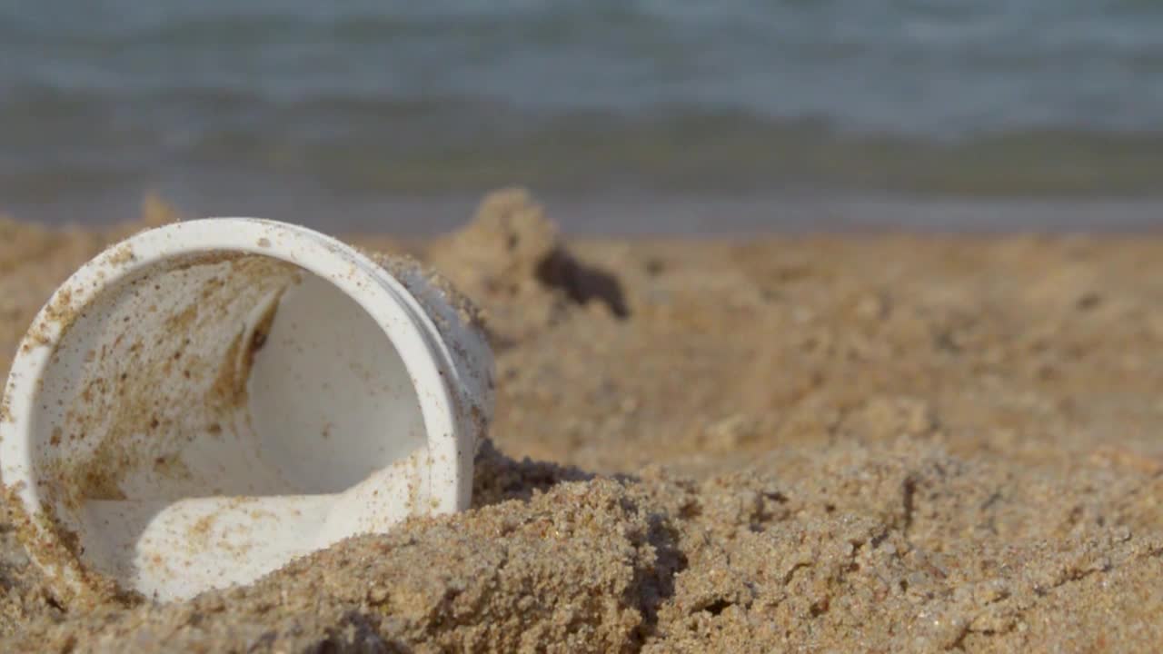 부드러운 와웨스가 해안을 강타하는 동안 아름다운 해변에 버려진 빈 플라스틱 컵, 오른쪽으로 이동