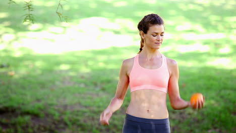 fit woman throwing an orange in the park