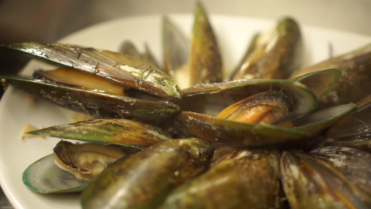 Colocando mejillones verdes de Nueva Zelanda recién cocidos en un plato en la cocina de un restaurante de lujo - Detalle en primer plano