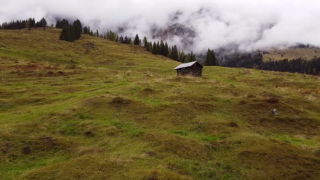 low aerial shot flying on grass mountain towards small wooden hut in austria