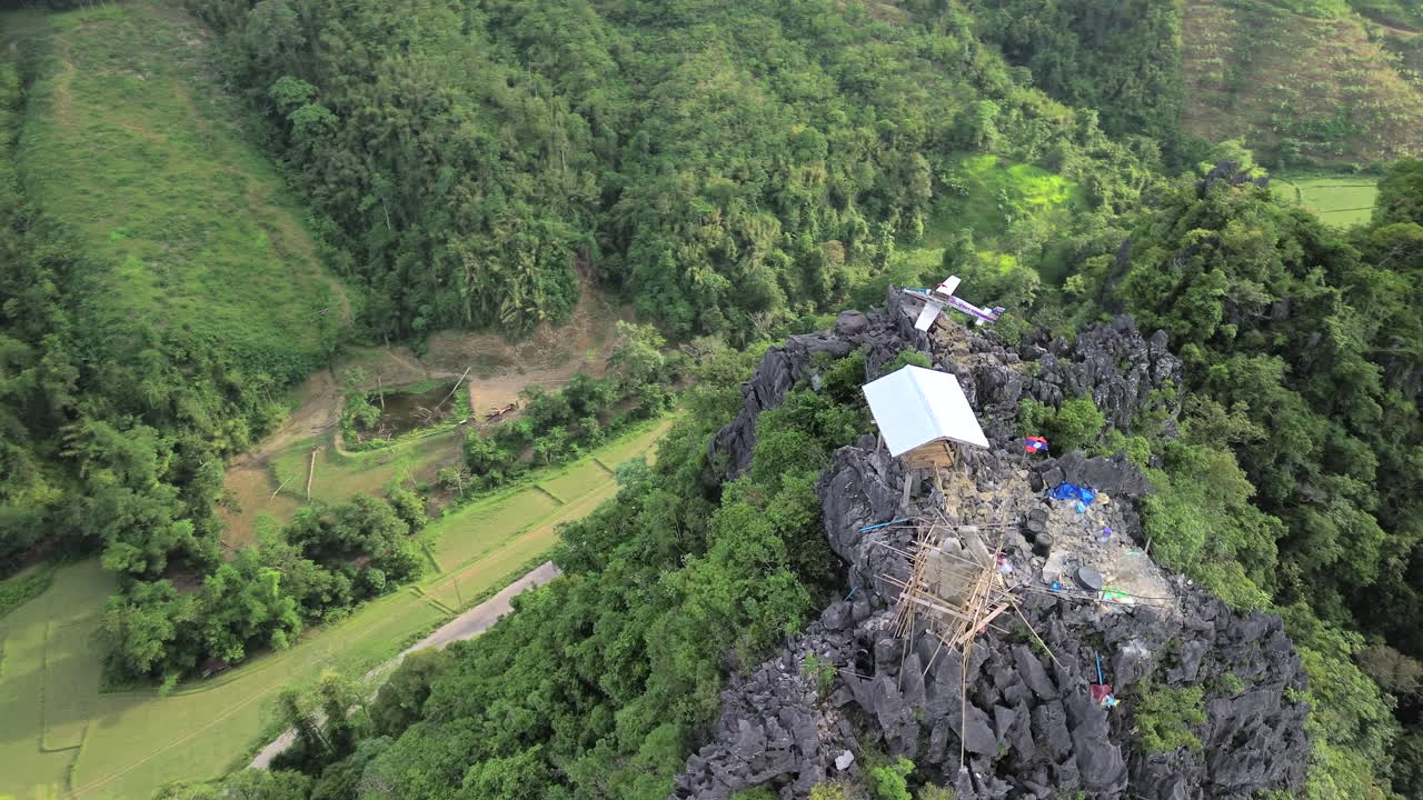 Vang Vieng viewpoint tower above jungle with tourists taking in the grand view, high angle aerial orbit above fields