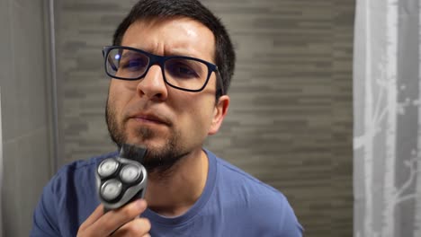 Man-shaving-his-beard-in-the-bathroom-looking-at-camera-like-if-it-was-a-mirror,-4K