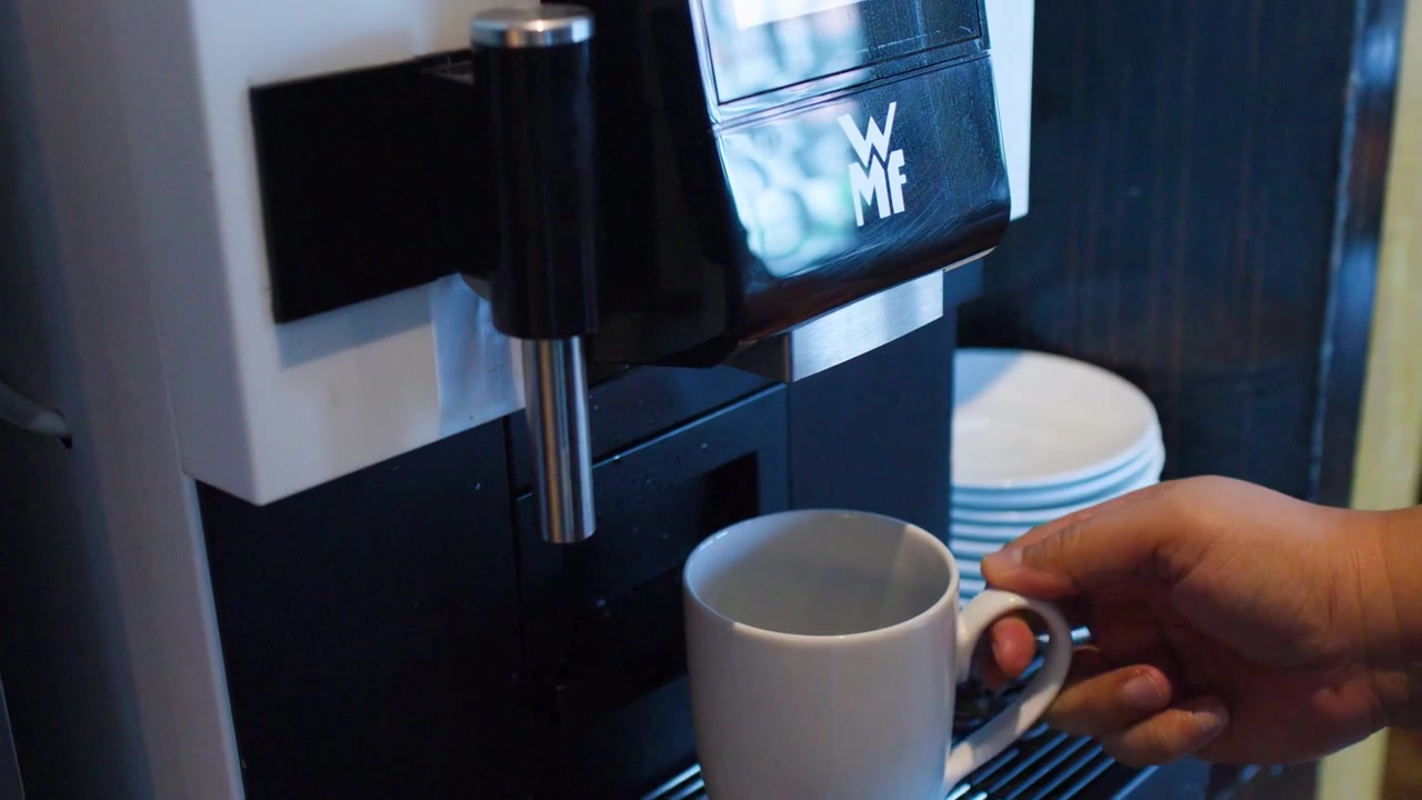 Primo piano di un uomo che prende una tazza bianca e la posiziona sotto una macchina da caffè espresso.
