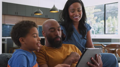 african american family with son sitting on sofa at home using digital tablet