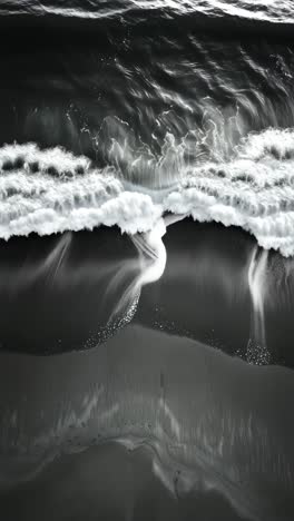 aerial view of waves crashing on a dark sandy beach, capturing the dynamic flow of water