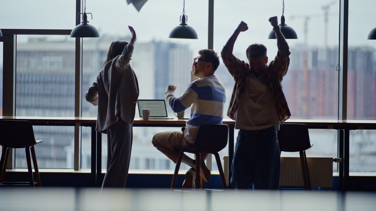 Startup group celebrating achievement throwing papers embracing at workplace