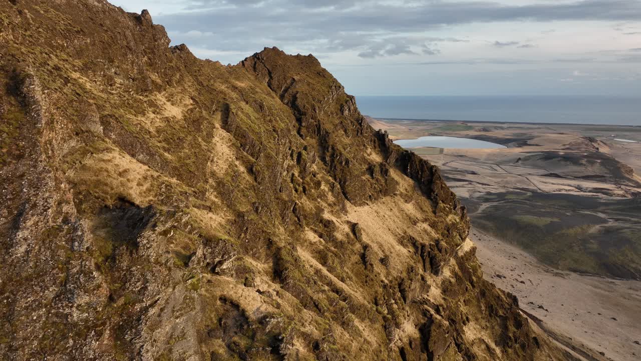 fotografía de un avión no tripulado de un acantilado escarpado y escarpado en búrfell, islandia, con vistas expansivas de distantes llanuras, lagos y el horizonte bajo un cielo nublado