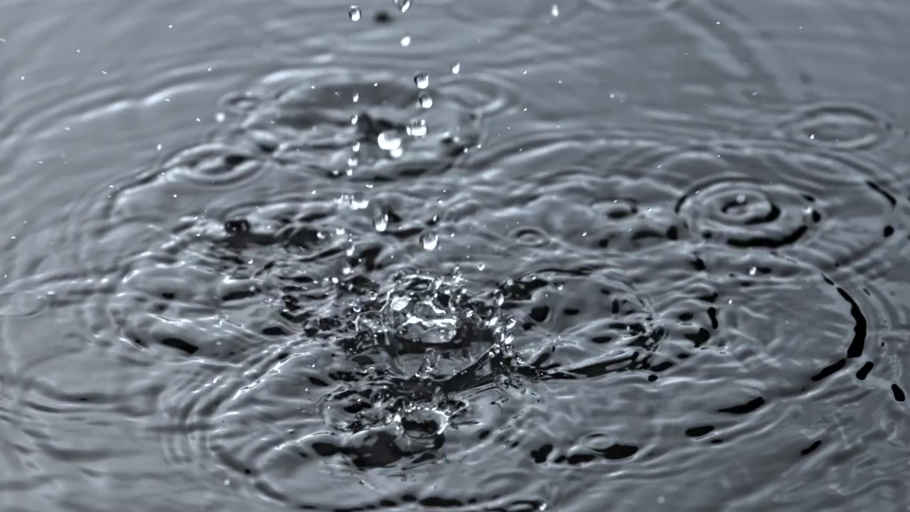 Wassertropfen fallen und spritzen in Zeitlupe auf dunkler Oberfläche