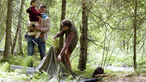 young family setting up tent near the river