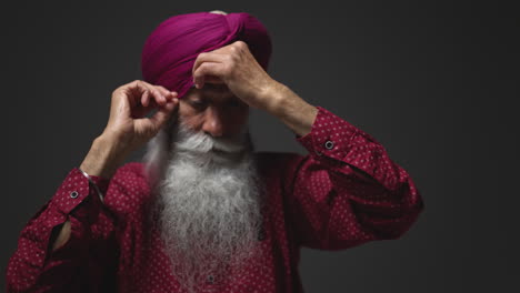 Primer-Plano,-Toma-De-Estudio-Con-Iluminación-Tenue-De-Un-Hombre-Sikh-Mayor-Con-Barba-Atando-Una-Tela-Para-Un-Turbante-Contra-Un-Fondo-Oscuro,-Filmado-En-Tiempo-Real-1