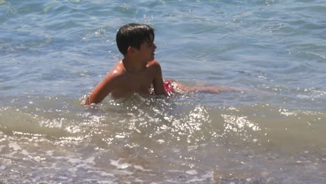 Medium-slow-motion-100fps-footage-of-8-years-old-caucasian-boy,-relaxing-at-the-seashore,-throwing-pebbles-in-the-sea,-isolated-static-shot