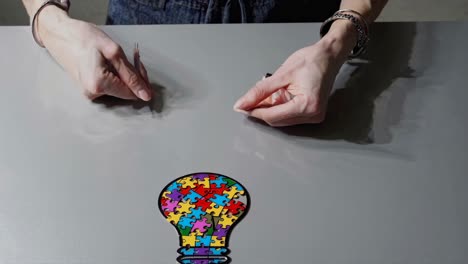 hands assembling a puzzle in the shape of a light bulb