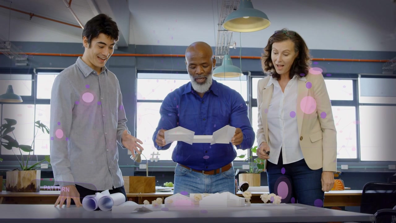Design team leaning over plans, man in blue unfolding prototype for review, pink circles overlaying