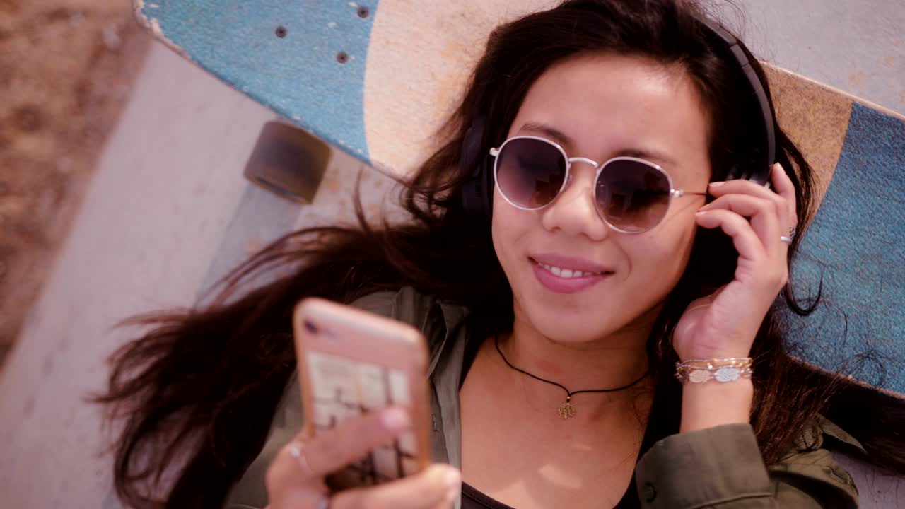 젊은 아시아 여성 스터 스케이트보더가 음악을 듣고 휴식을 취하고 있습니다.