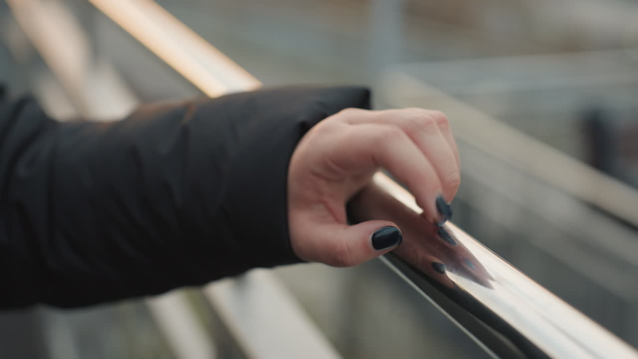 Closeup hand on railing with dark polish and winter sleeve, fingertip tapping on reflective chrome, subtle rhythmic movement like finger dance, intimate cinematic detail, shallow depth and soft urban